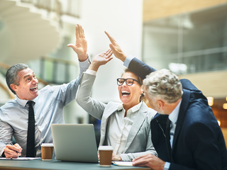 Ecstatic group of colleagues gathering at a meeting around a table in the lobby of an office building