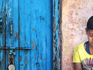 Boy sitting on steps near the door with rusty lock.
